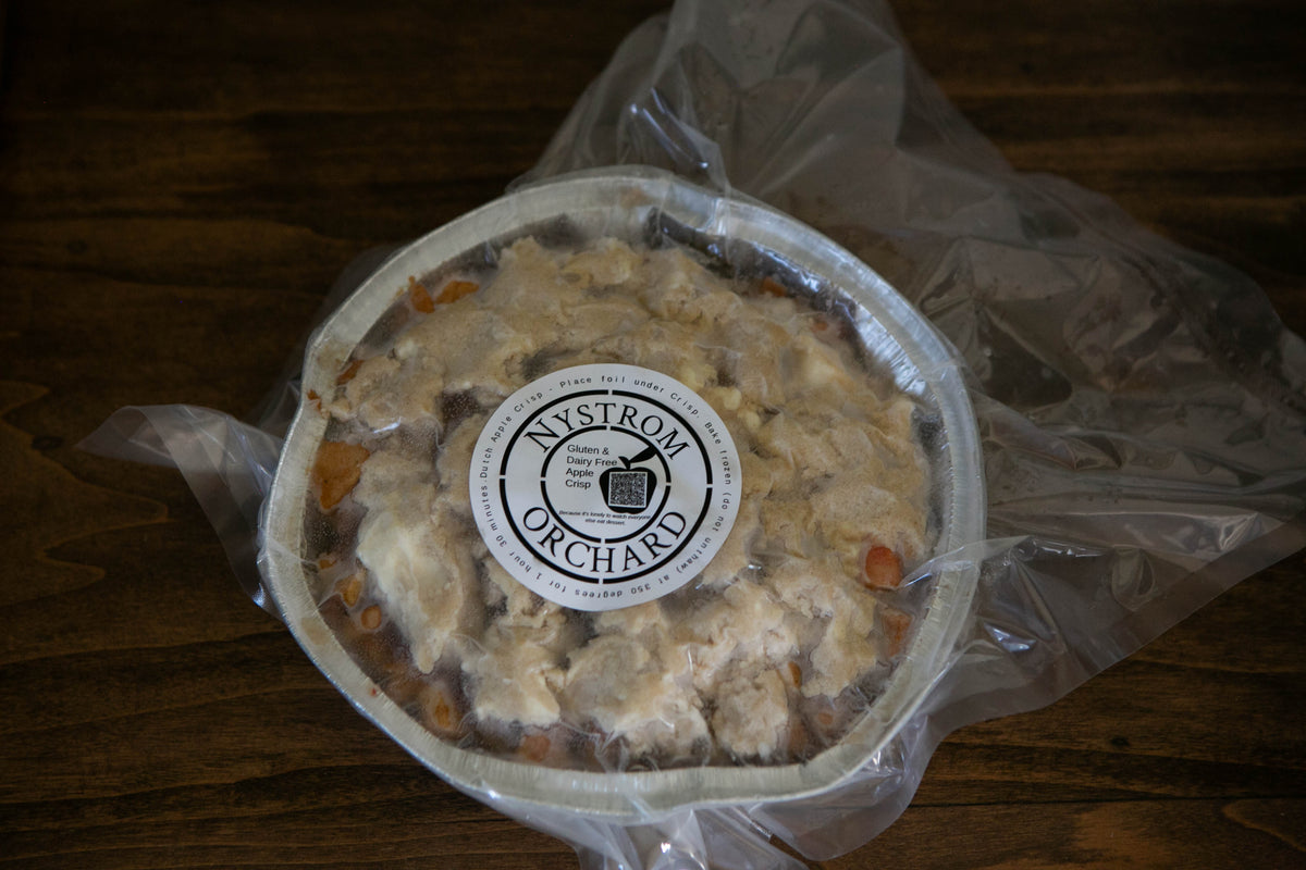 A vacuum sealed foil pan of gluten and dairy free apple crisp on a wooden surface. Made in the kitchen of Nystrom Orchard in Worthington Minnesota.