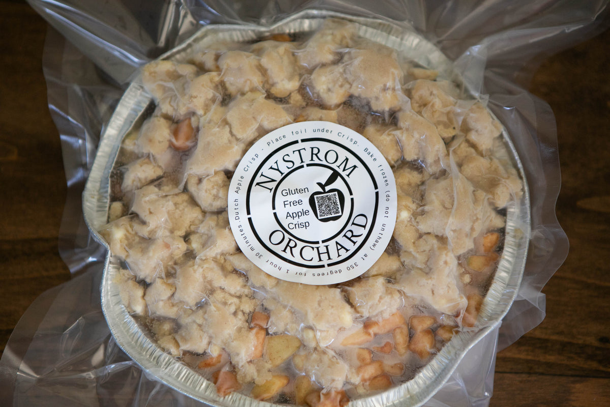 A foil pan with gluten free apple crisp frozen and pre-packaged on a wooden surface with a Nystrom Orchard label. Made in the kitchen of Nystrom Orchard in Worthington Minnesota.