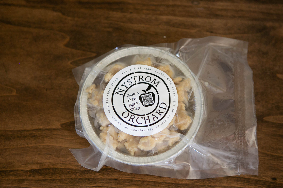 A packaged frozen mini pan of gluten free apple crisp on a wooden surface. Made in the kitchen of Nystrom Orchard in Worthington Minnesota.