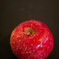 A single red apple with a slight pinkish hue and natural patterns, displayed against a dark background. Picked at Nystrom Orchard in Worthington Minnesota.