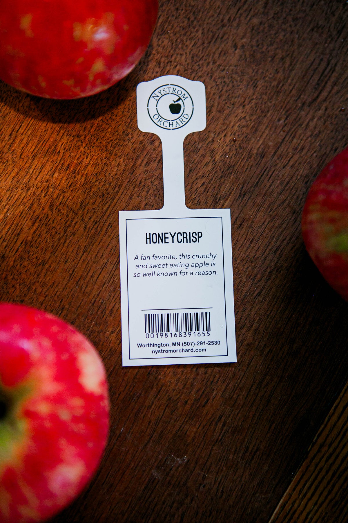 Honeycrisp tag with honeycrisp apples on a wooden surface. Picked at Nystrom Orchard in Worthington Minnesota.