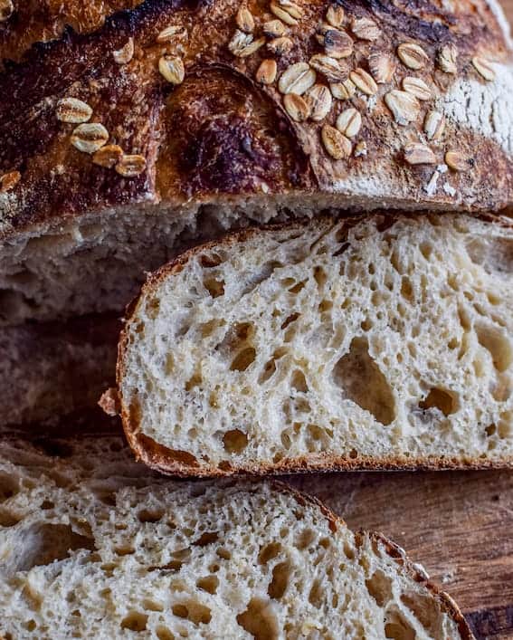 Rustic loaf of honey oat sourdough bread sliced off of a main loaf on a wooden surface. Baked in the kitchen at Nystrom Orchard in Worthington Minnesota. 