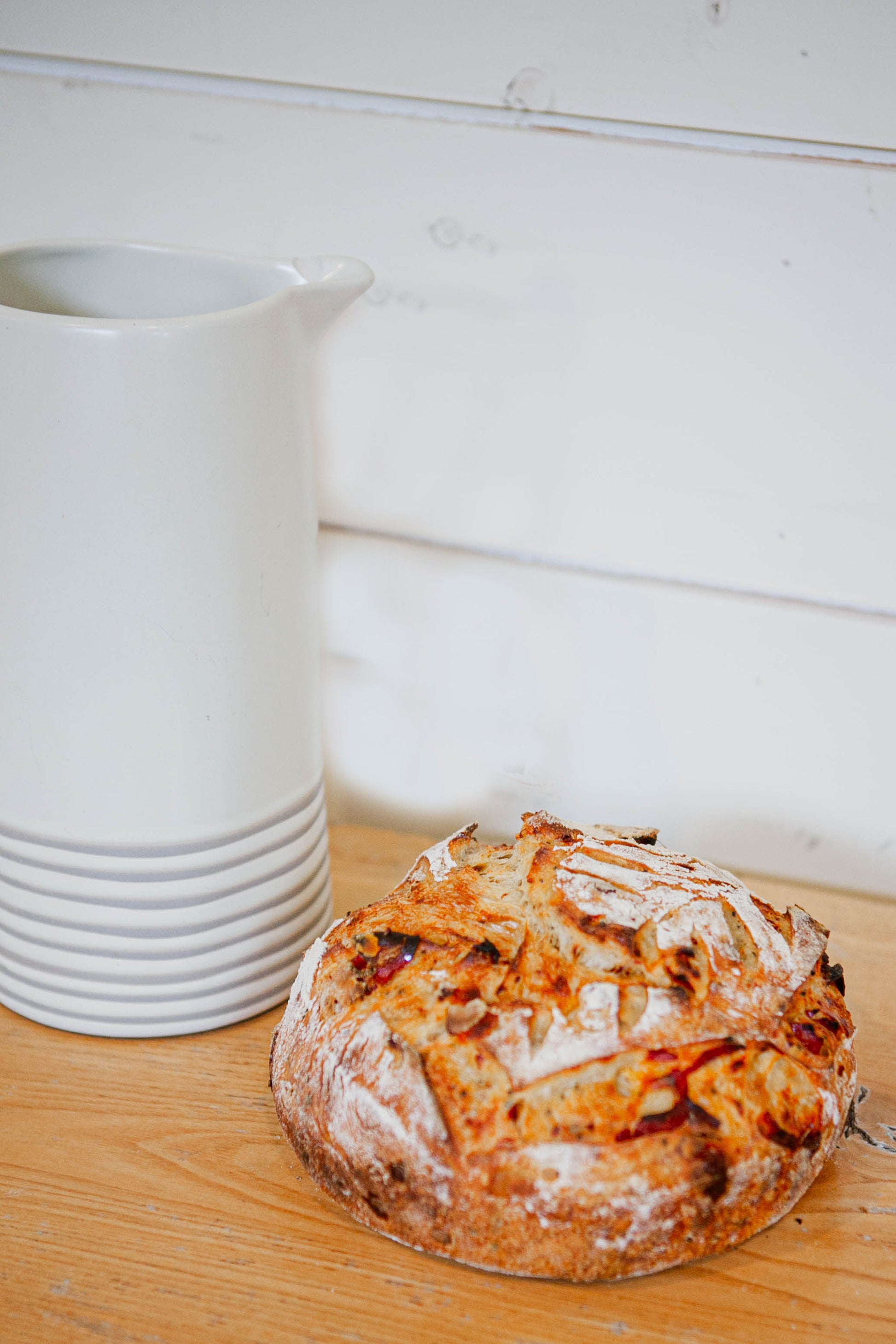 Rustic loaf of hot honey gouda sourdough bread on a wooden surface with white ceramic containers in the background. Bake in the kitchen of Nystrom Orchard in Worthington Minnesota.