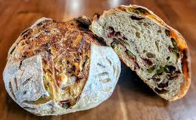 Loaf of jalapeno bacon cream cheese sourdough bread with a cut section revealing interior texture on a wooden surface. Baked in the kitchen at Nystrom Orchard in Worthington Minnesota.