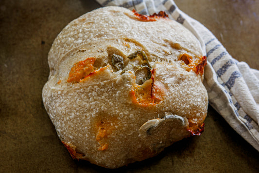 Rustic loaf of sourdough bread with cheddar and jalapenos on a dark surface with a blue and white cloth. Baked in the kitchen at Nystrom Orchard in Worthington Minnesota. 