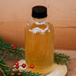 Glass bottle with lemon ginger syrup and a black cap on a wooden surface with a wooden background, greenery and red berries. Made in the kitchen at Nystrom Orchard in Worthington Minnesota.