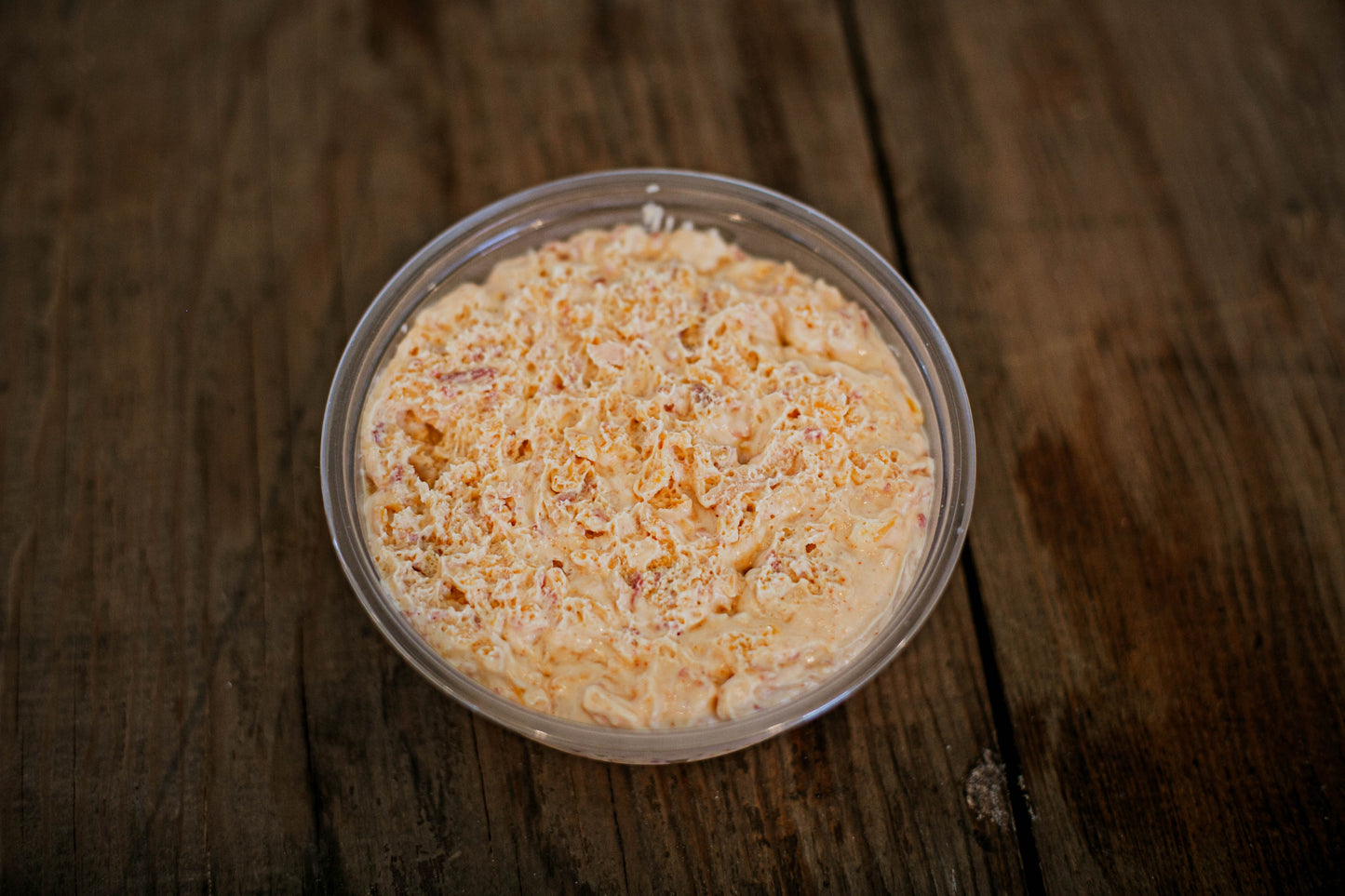 Container of maple bacon cheese dip on a wooden surface.  Made in the kitchen of Nystrom Orchard in Worthington Minnesota.