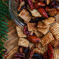 Nuts, cranberries, and rice chex mixed together in a snack mix spilling out of a cup onto a wooden surface with greenery. Made by the kitchen at Nystrom Orchard in Worthington Minnesota.