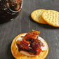 Cracker with cream cheese and maple bacon onion jam on a dark surface. Made in the kitchen at Nystrom Orchard in Worthington Minnesota.