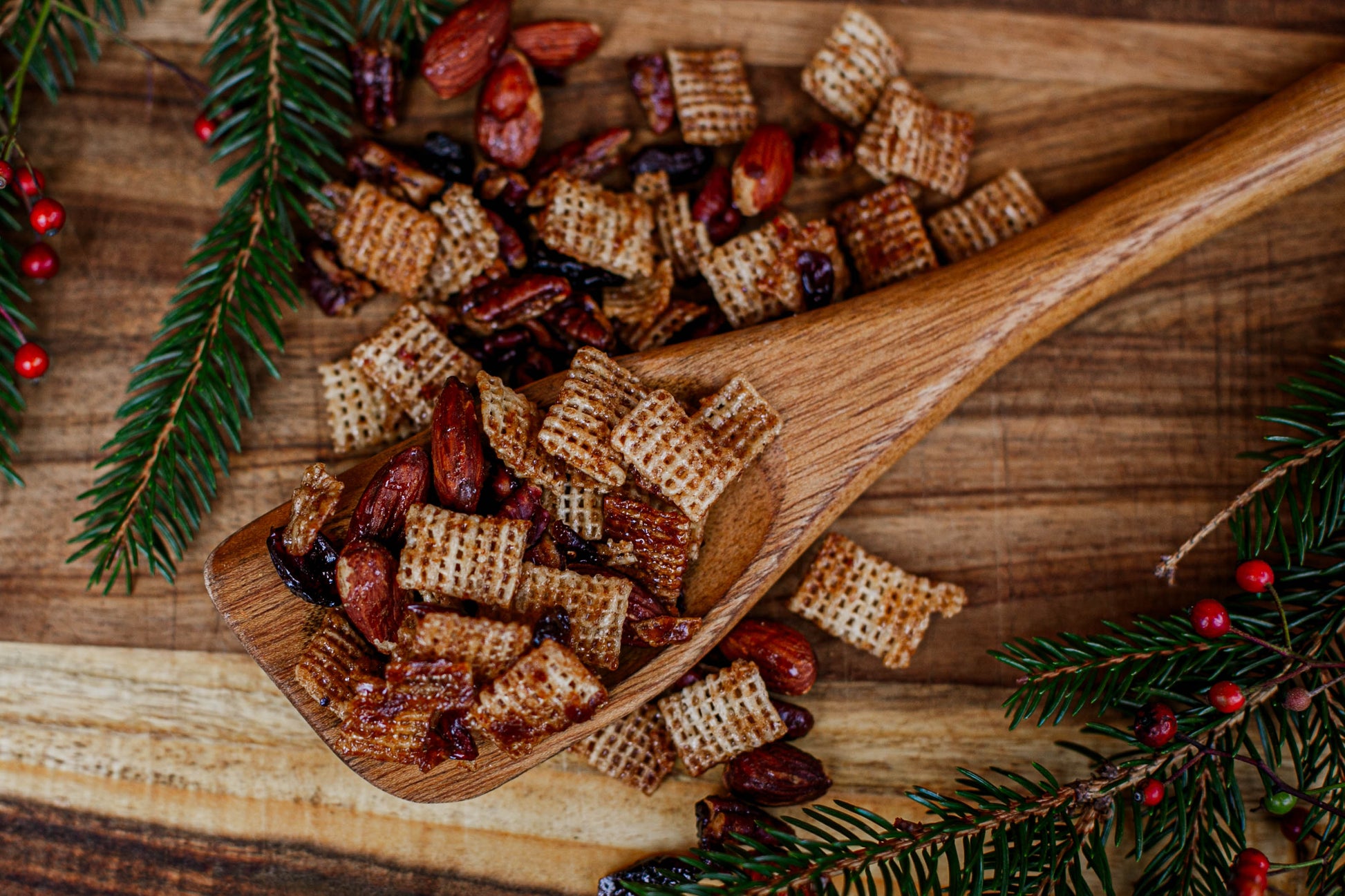 Wooden spoon filled with maple pecan snack mix on a wooden surface with Christmas decorations. Made in the kitchen at Nystrom Orchard in Worthington Minnesota.