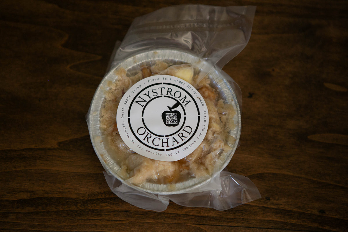 Mini apple crisp frozen and vacuum sealed in a foil pan on a wooden surface. Made in the kitchen of Nystrom Orchard in Worthington Minnesota.