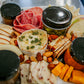 Platter of assorted meats, cheeses, fruits, and nuts with small jars on a white plate. Made in the kitchen of Nystrom Orchard in Worthington Minnesota.