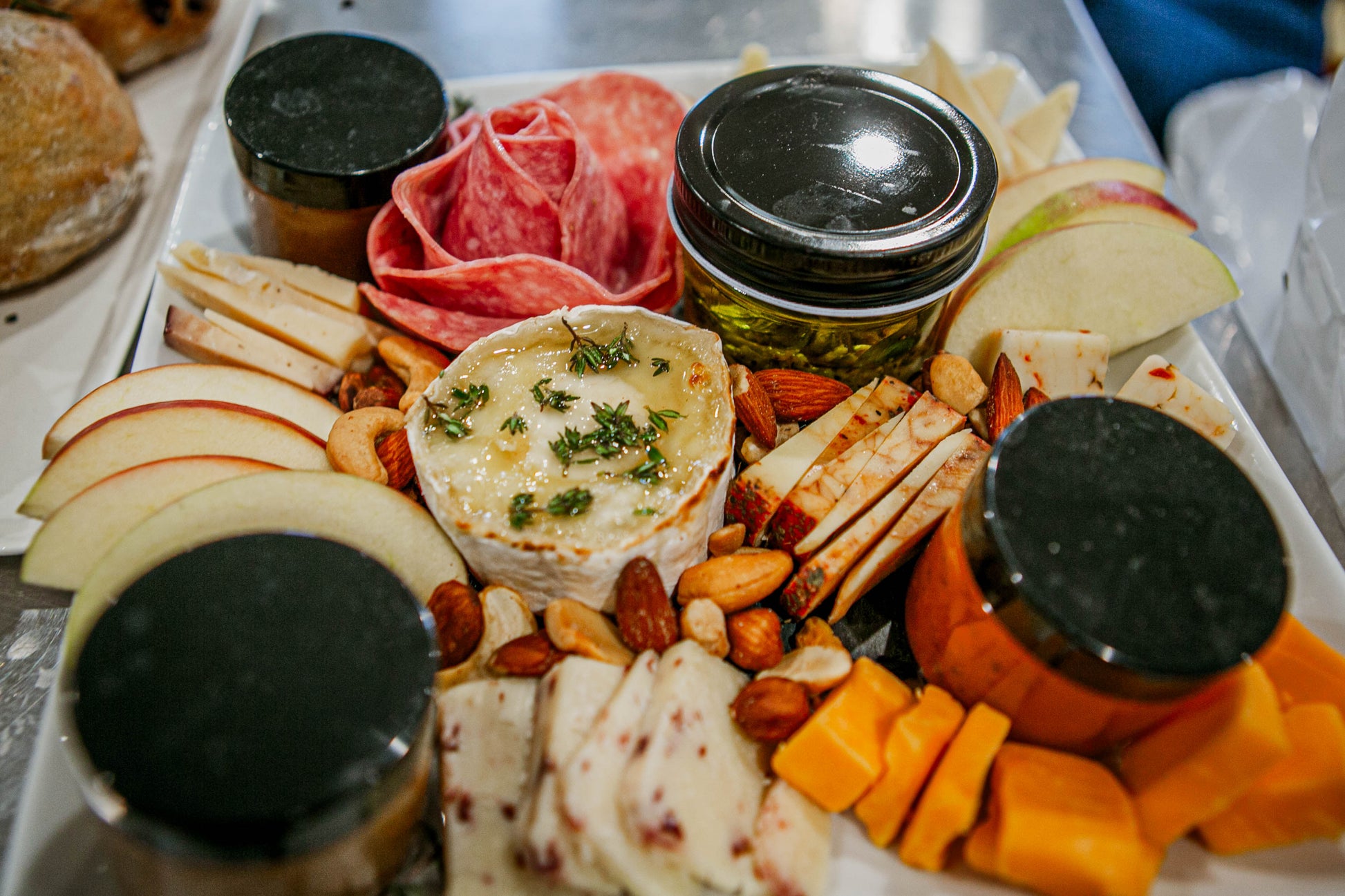 Platter of assorted meats, cheeses, fruits, and nuts with small jars on a white plate. Made in the kitchen of Nystrom Orchard in Worthington Minnesota.
