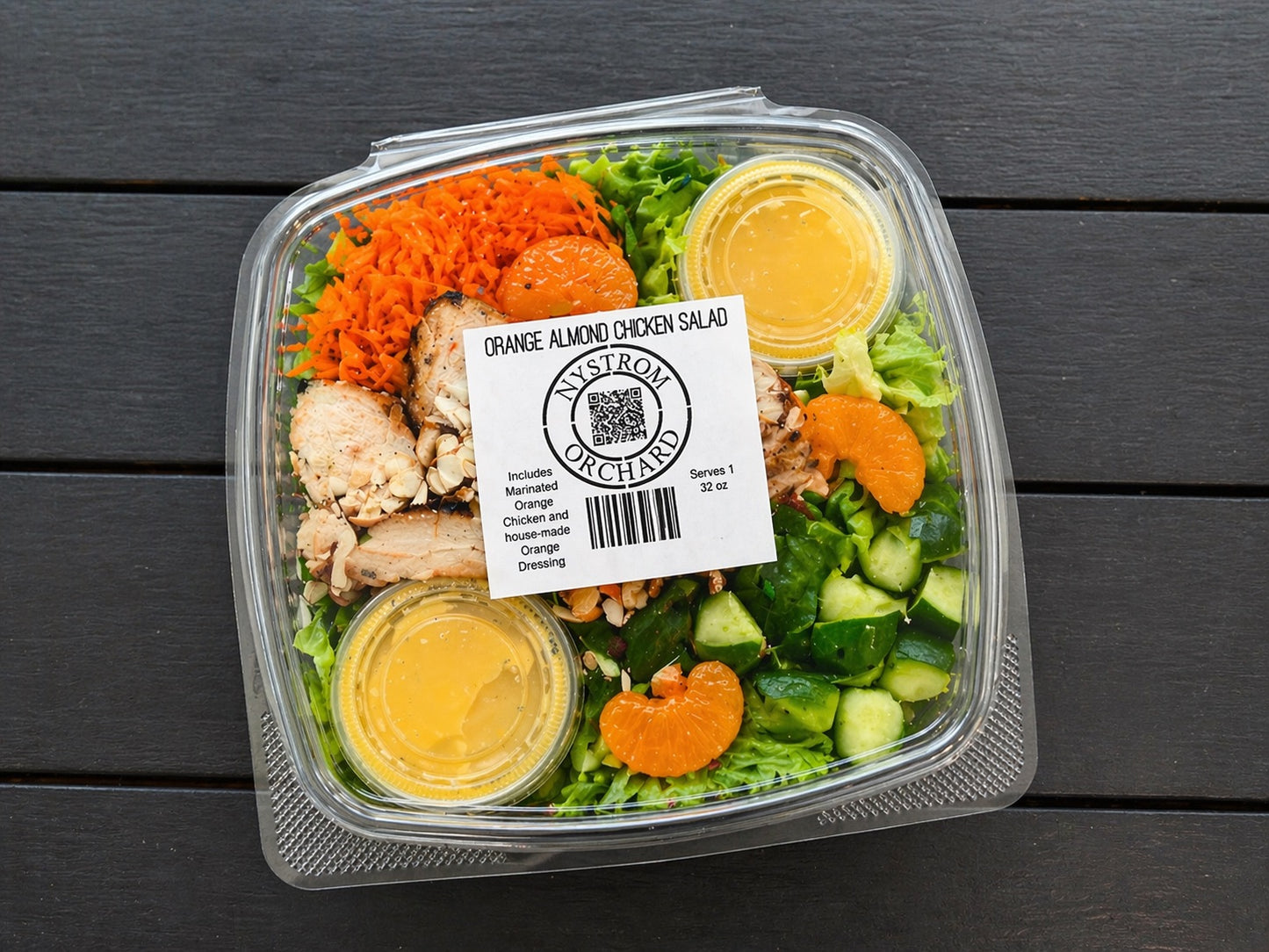 Plastic container of orange almond chicken salad with citrus dressing with visible branding on a wooden surface. Made fresh in the kitchen of Nystrom Orchard in Worthington Minnesota.