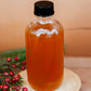 Glass bottle with Nystrom orchard signature syrup with a black cap on a wooden surface with greenery and red berries. Made in the kitchen at Nystrom Orchard in Worthington Minnesota.