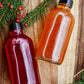 Two bottles of cider syrup on a wooden surface with Christmas decorations. Made in the kitchen at Nystrom Orchard in Worthington Minnesota.
