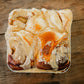 Foil pan of four sourdough cinnamon rolls covered in browned butter frosting on a wooden surface. Baked in the kitchen of Nystrom Orchard in Worthington Minnesota.