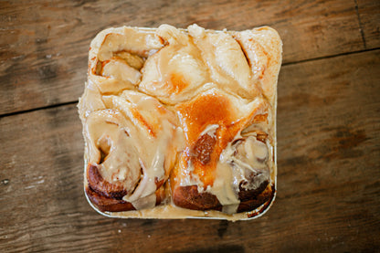 Foil pan of four sourdough cinnamon rolls covered in browned butter frosting on a wooden surface. Baked in the kitchen of Nystrom Orchard in Worthington Minnesota.