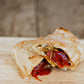 Soft pretzel wrap cut in half to show its full of pepperoni and cheese on a wooden cutting board. Made in the kitchen of Nystrom Orchard in Worthington Minnesota.