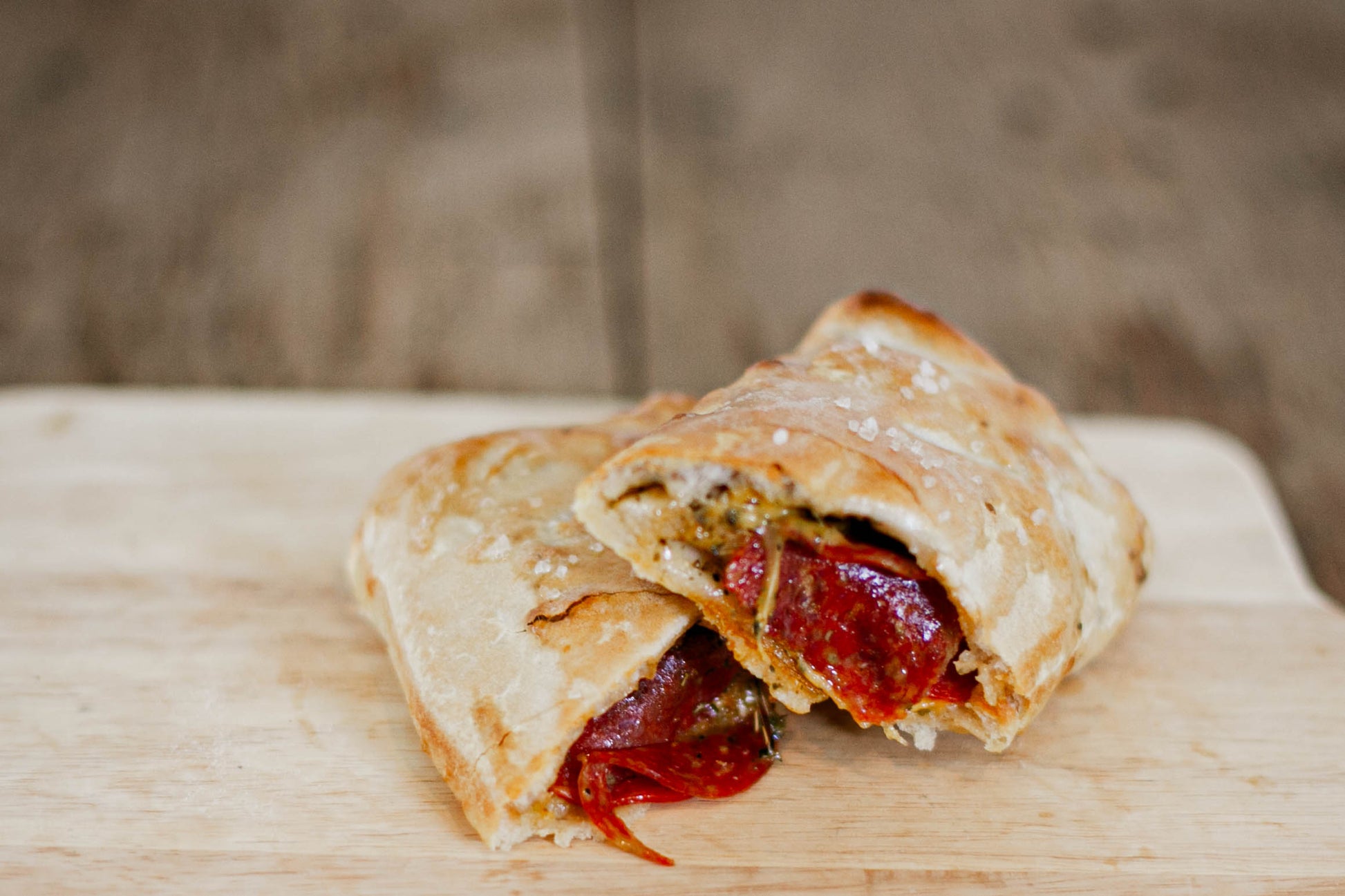 Soft pretzel wrap cut in half to show its full of pepperoni and cheese on a wooden cutting board. Made in the kitchen of Nystrom Orchard in Worthington Minnesota.