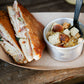 Grilled pork sandwich with corn chowder and homemade croutons in a brown paper boat on a table. Made in the kitchen or Nystrom Orchard in Worthington Minnesota.