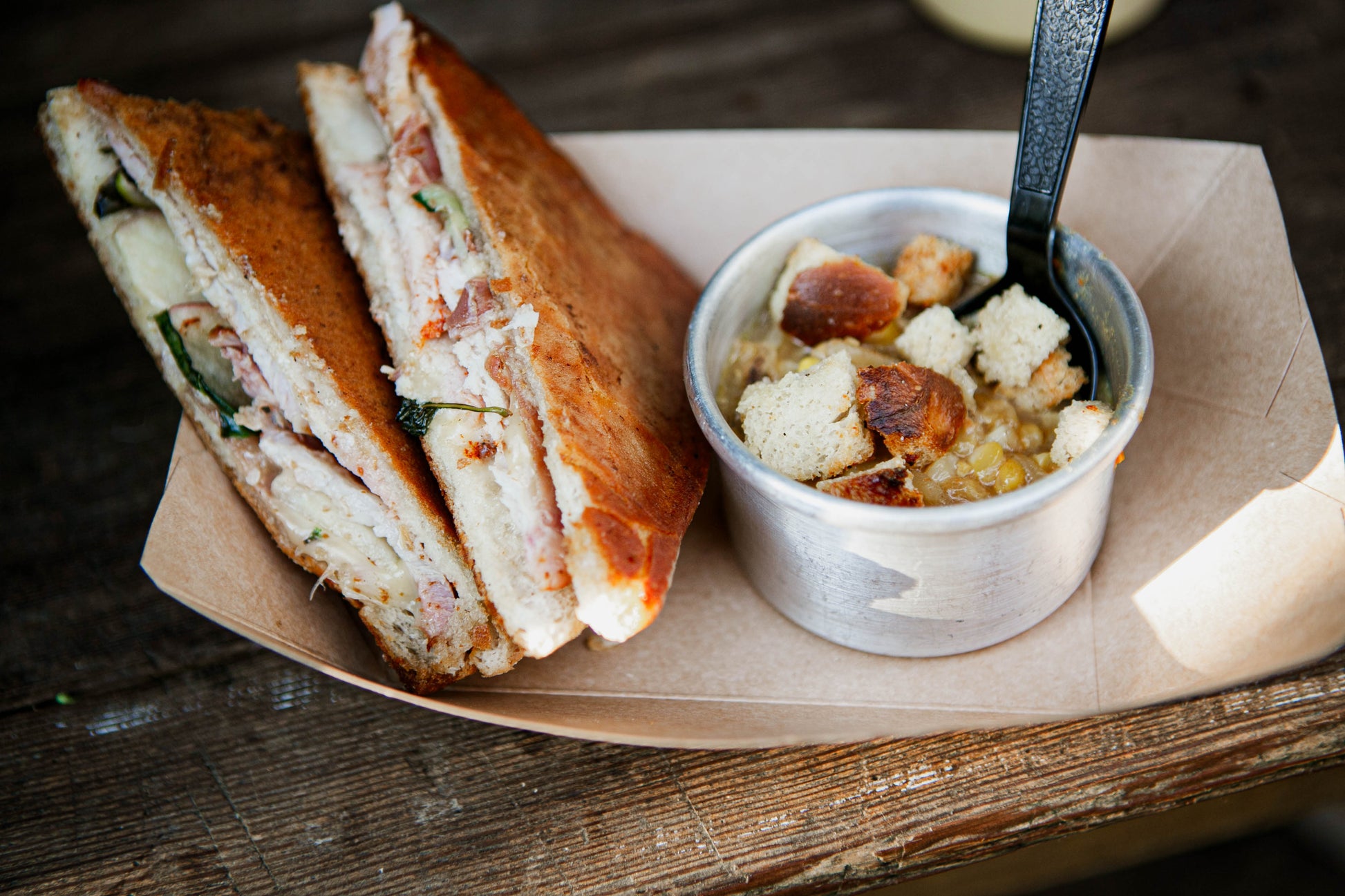 Grilled pork sandwich with corn chowder and homemade croutons in a brown paper boat on a table. Made in the kitchen or Nystrom Orchard in Worthington Minnesota.