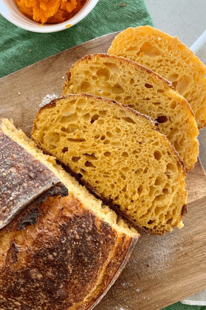 Rustic sliced pumpkin and sage sourdough bread sliced on a cutting board with pumpkin and a green towel. Made in the kitchen at Nystrom Orchard in Worthington Minnesota.