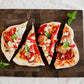 Roasted red pepper pizza, smoked sausage, blue cheese and basil flatbread on a wooden cutting board on a white surface. Baked in the kitchen of Nystrom Orchard in Worthington Minnesota.