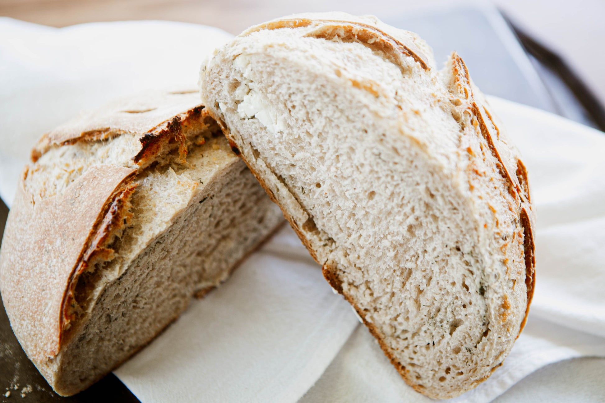Rustic artisan rosemary and gouda sourdough bread cut in half and propped up on each other on a white cloth. Baked in the kitchen at Nystrom Orchard in Worthington Minnesota.