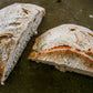 A loaf of rustic sourdough bread cut in half on a dark surface. Baked in the kitchen of Nystrom Orchard in Worthington Minnesota.