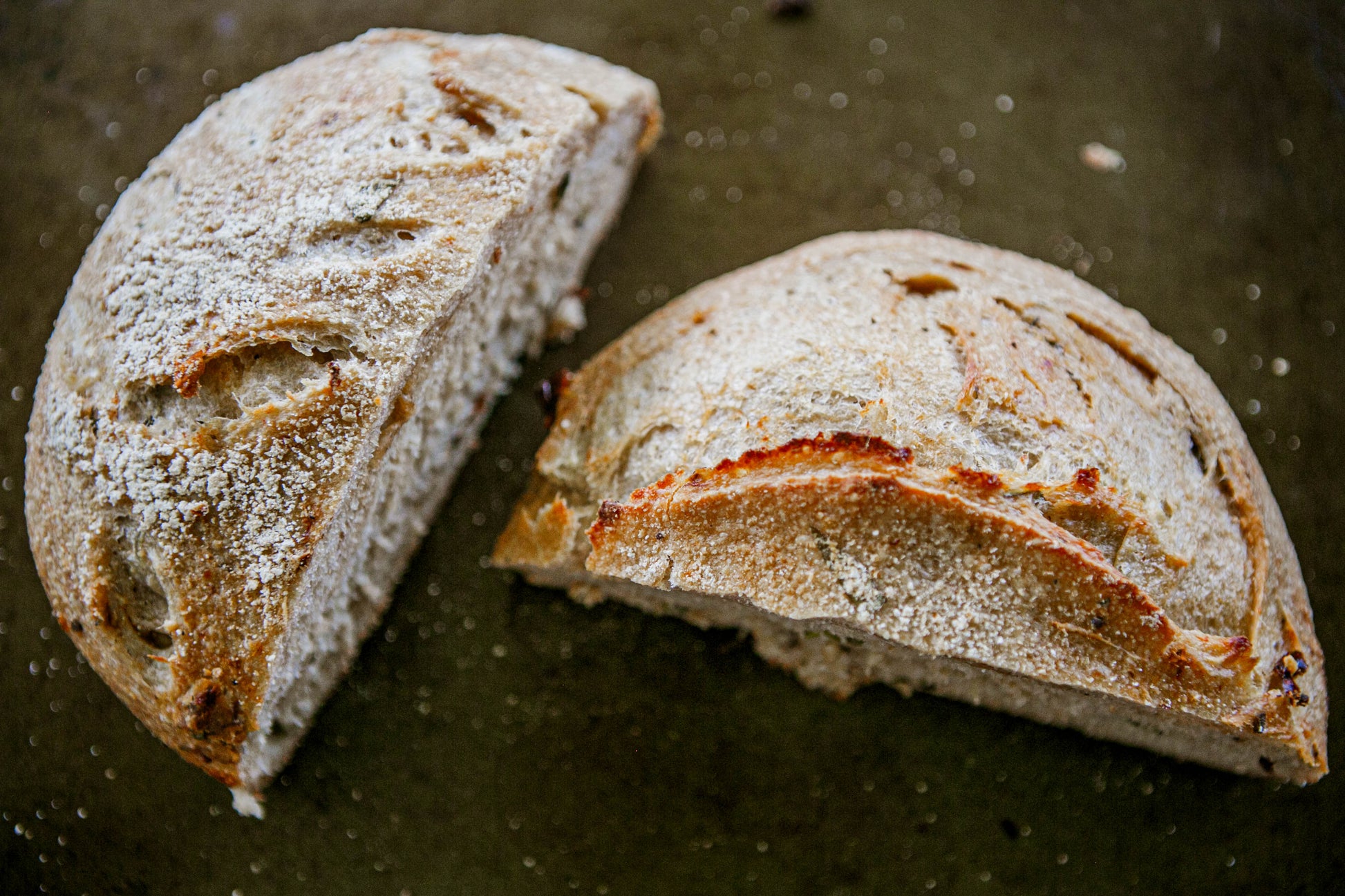 A loaf of rustic sourdough bread cut in half on a dark surface. Baked in the kitchen of Nystrom Orchard in Worthington Minnesota.