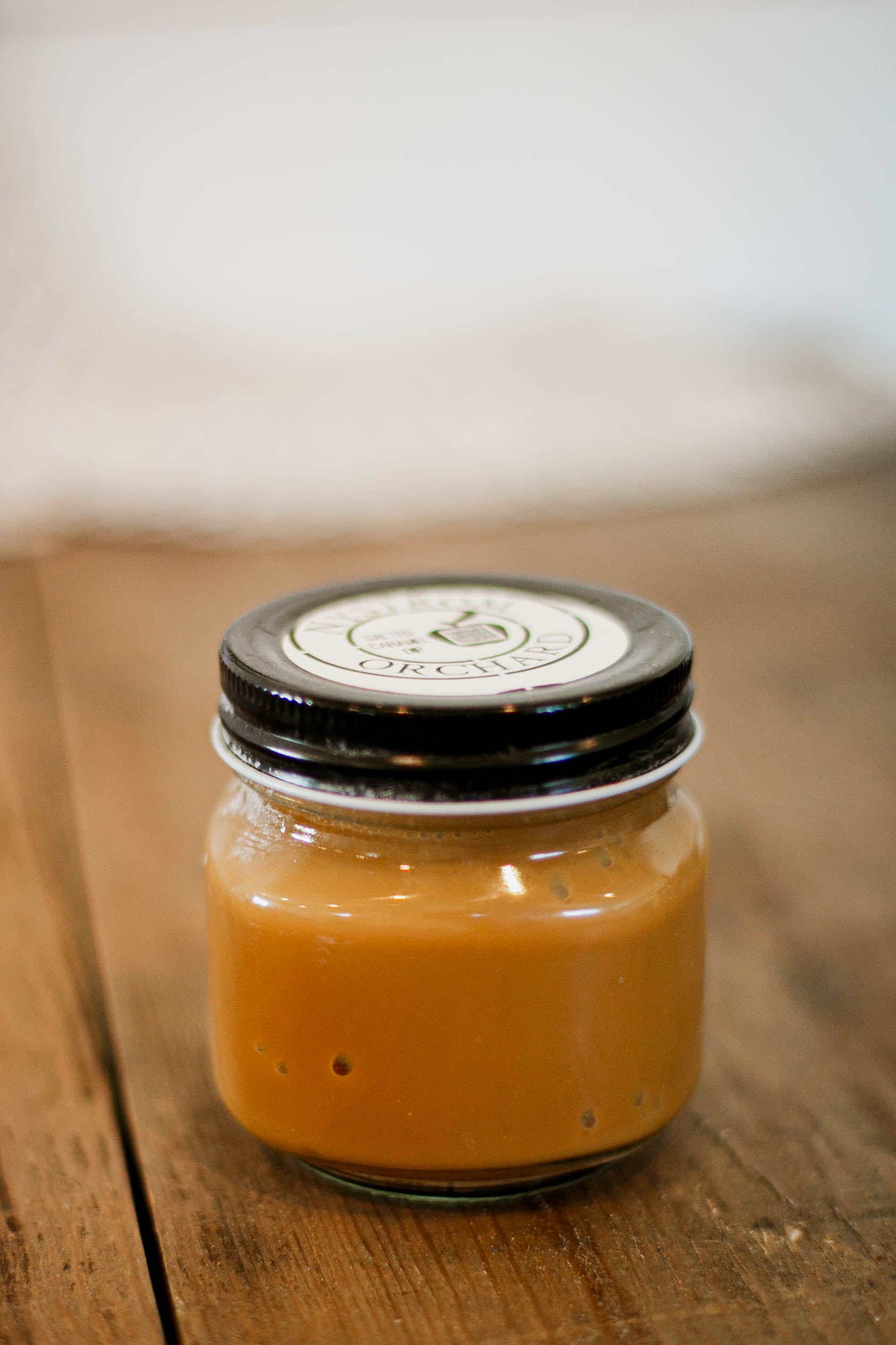 Salted caramel apple dip in a 8 oz jar on a wooden surface with white background. Made in the kitchen of Nystrom Orchard in Worthington Minnesota.