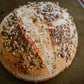 Freshly baked seeded sourdough loaf with a crust covered with seeds on a dark background. Baked in the kitchen of Nystrom Orchard in Worthington Minnesota.