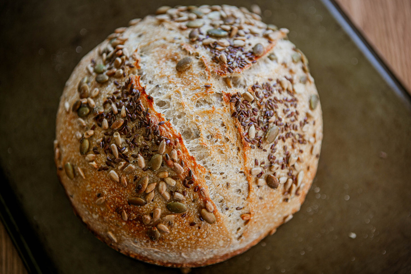 Freshly baked seeded sourdough loaf with a crust covered with seeds on a dark background. Baked in the kitchen of Nystrom Orchard in Worthington Minnesota.