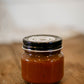 Glass 8 oz jar of apple butter with a black lid on a wooden surface. Made in the kitchen of Nystrom Orchard in Worthington Minnesota.