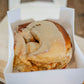 Single sourdough cinnamon roll in a white box on a cutting board with a wooden background. Baked in the kitchen of Nystrom Orchard in Worthington Minnesota.