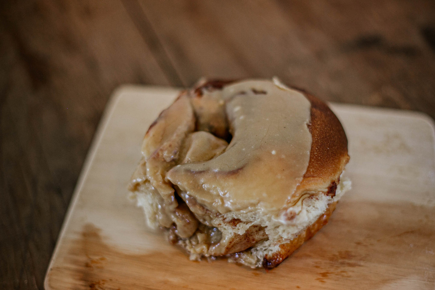 Close up of a sourdough cinnamon roll with browned butter icing on a wooden cutting board. Baked in the kitchen of Nystrom Orchard in Worthington Minnesota.
