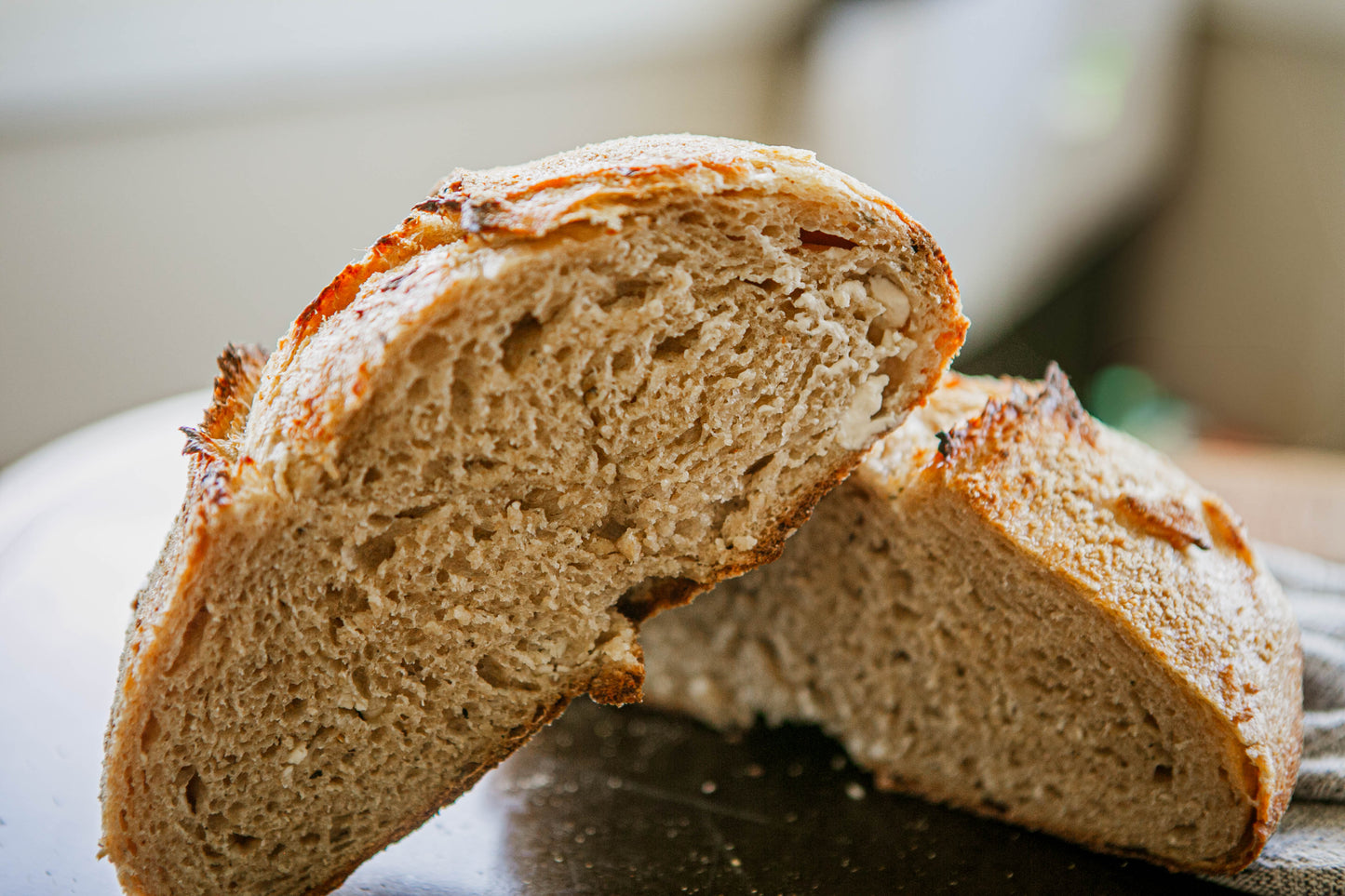 Close up of a rustic loaf of tomato basil sourdough bread cut in half on a dark surface with a blurry background. Baked in the kitchen of Nystrom Orchard in Worthington Minnesota.  