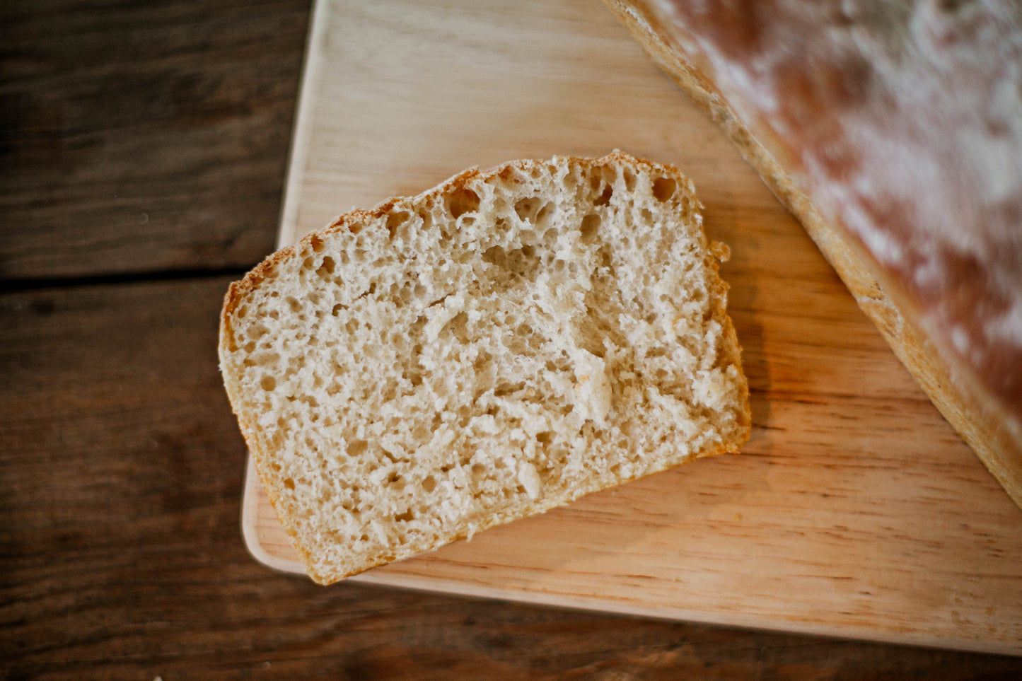A slice of sourdough sandwich bread on a wooden cutting board with a blurred loaf in the background. Baked in the kitchen at Nystrom Orchard in Worthington Minnesota.