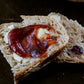 Two slices of cranberry cream cheese sourdough on a dark surface the slices are spread with butter and jam.  Baked in the kitchen at Nystrom Orchard in Worthington Minnesota.