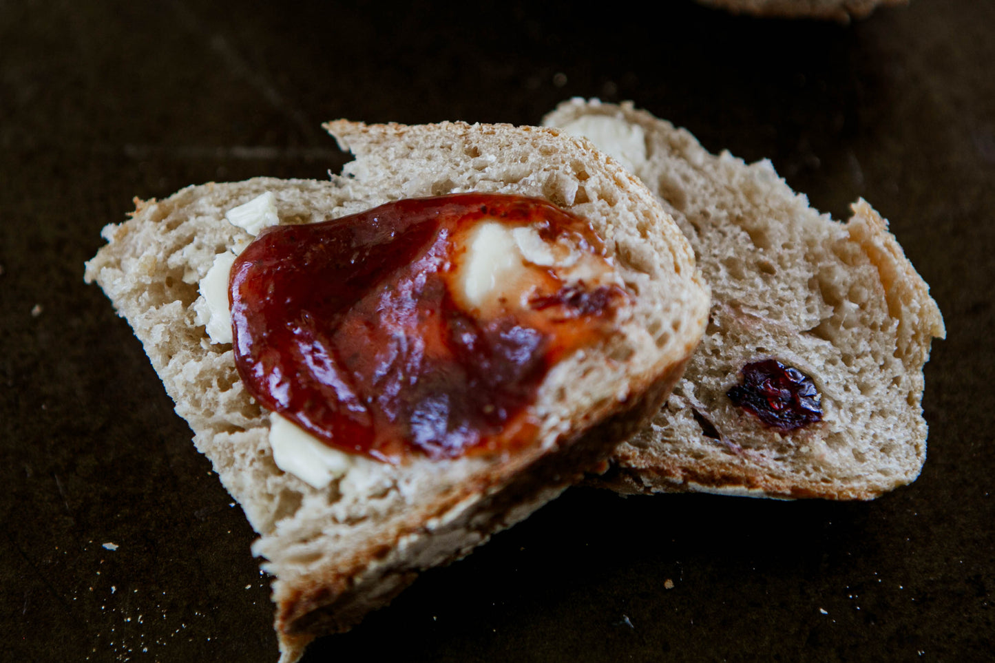 Two slices of cranberry cream cheese sourdough on a dark surface the slices are spread with butter and jam.  Baked in the kitchen at Nystrom Orchard in Worthington Minnesota.