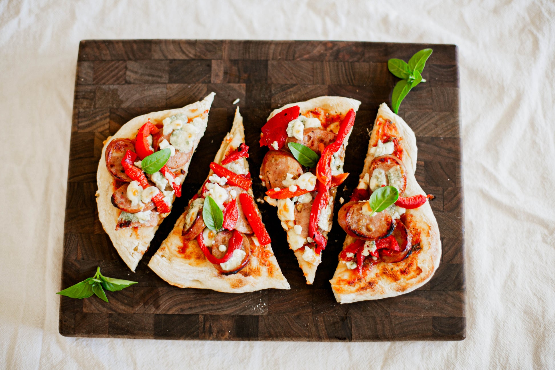 Roasted red pepper sausage blue cheese flatbread topped with basil on a wooden cutting board on a white background. Baked in the kitchen of Nystrom Orchard in Worthington Minnesota. 