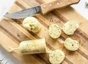 Smokey herbed butter log on a wooden cutting board with a knife. Made in the kitchen of Nystrom Orchard in Worthington Minnesota.