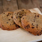 Three chocolate chip cookies on a wooden cutting board with a blurred wooden background.  Baked in the kitchen of Nystrom Orchard in Worthington Minnesota.