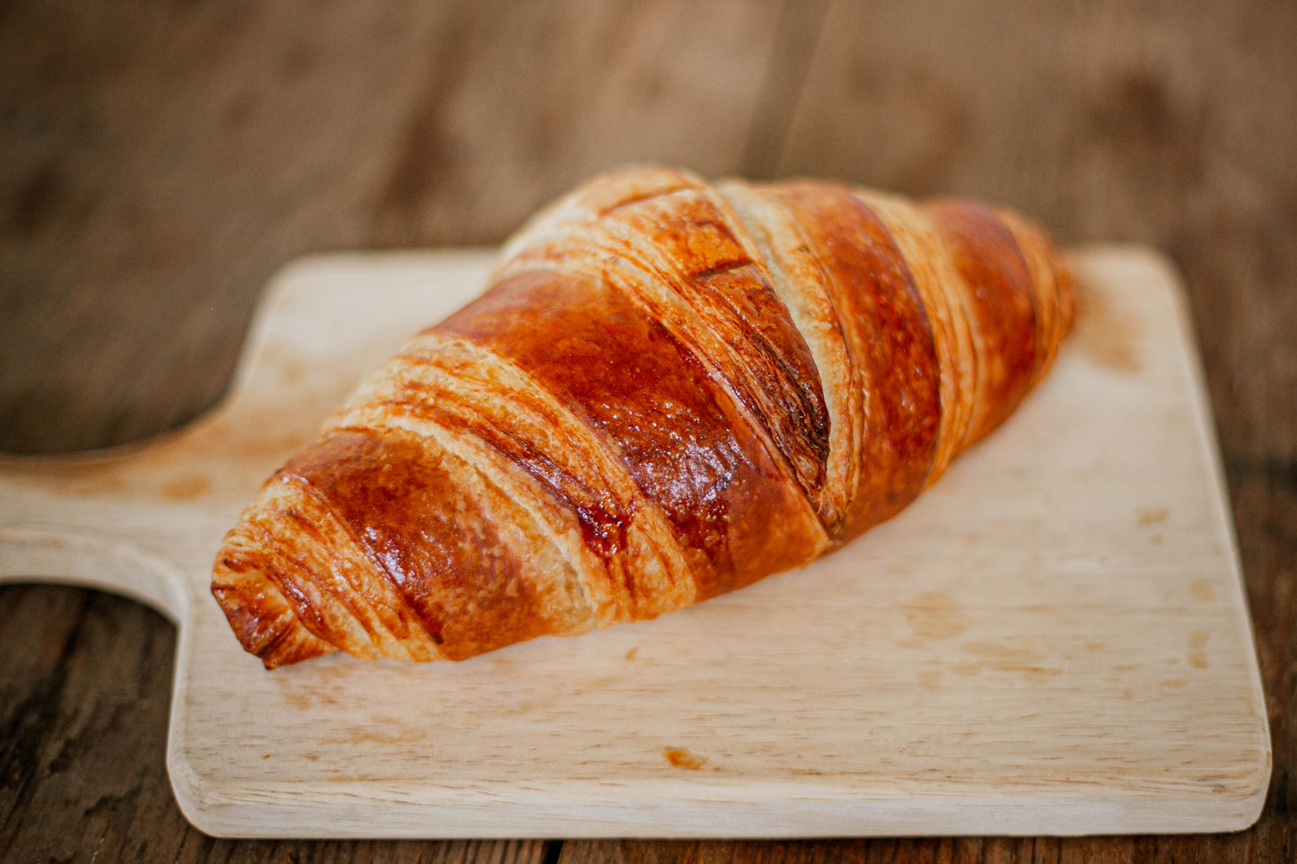 Homemade sourdough croissant on a wooden cutting board with a blurred wooden background. Baked in the kitchen of Nystrom Orchard in Worthington Minnesota.