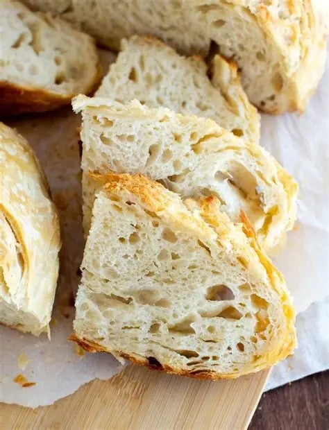 Close up of artisan croissant sourdough loaf of bread sliced so you can see the airy buttery texture on a white parchment paper. Baked in the kitchen of Nystrom Orchard in Worthington Minnesota.