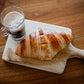 Homemade sourdough croissant on a wooden cutting board with a glass of coffee on a wooden surface. Baked in the kitchen of Nystrom Orchard in Worthington Minnesota.