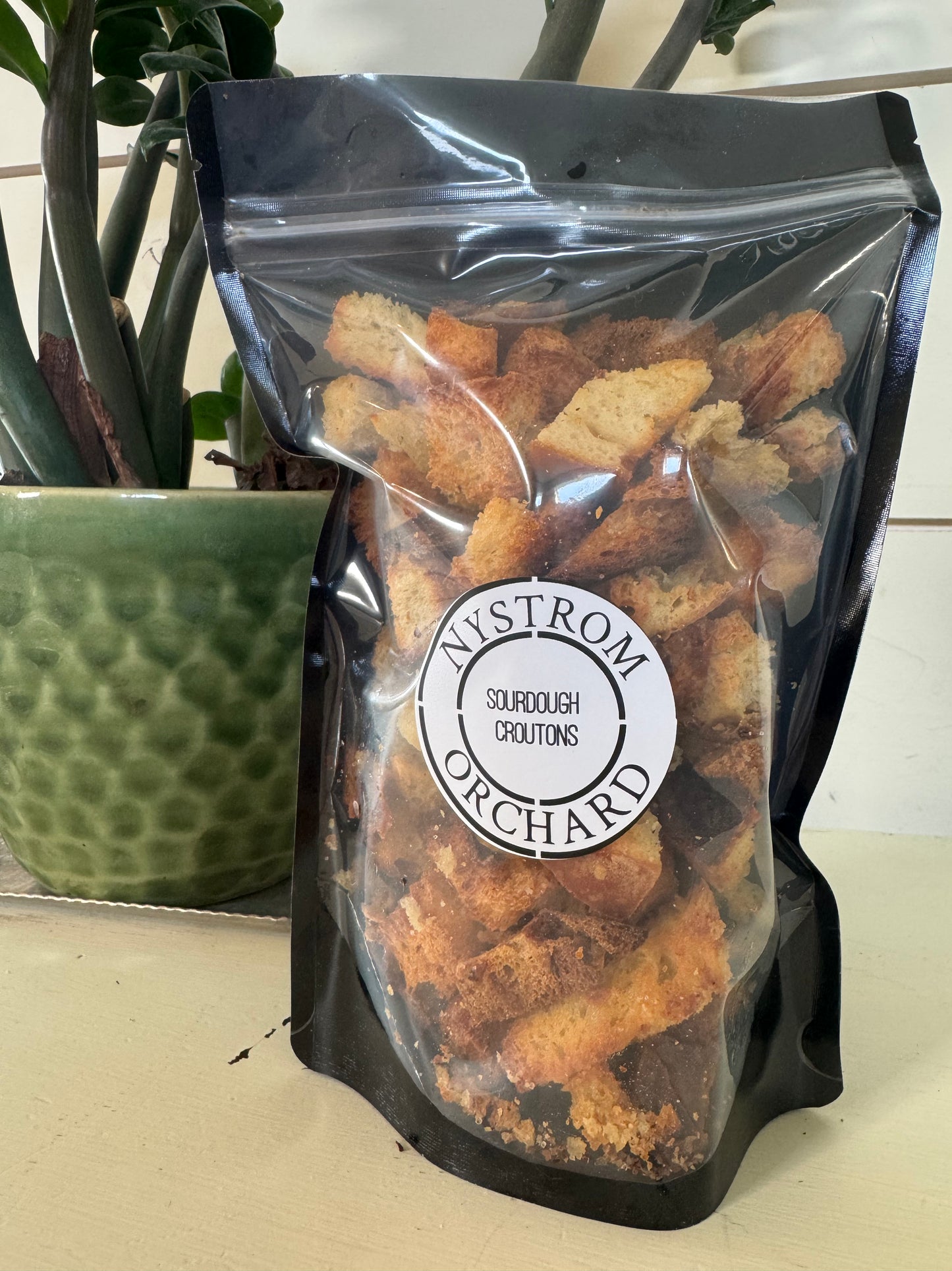 Bag of sourdough croutons with a plant in the background. Baked in the kitchen at Nystrom Orchard in Worthington Minnesota. 