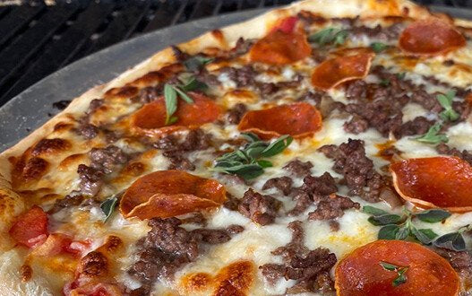 Sourdough pizza with sauce, cheese, pepperoni, fresh herbs and beef on a stone inside a grill. Made in the kitchen at Nystrom Orchard in Worthington Minnesota.