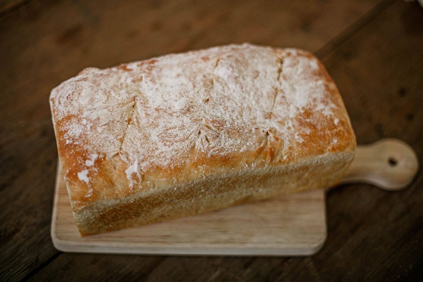 Loaf of sourdough sandwich bread baked in a rectangle pan on a wooden cutting board. Baked in the kitchen at Nystrom Orchard in Worthington Minnesota.